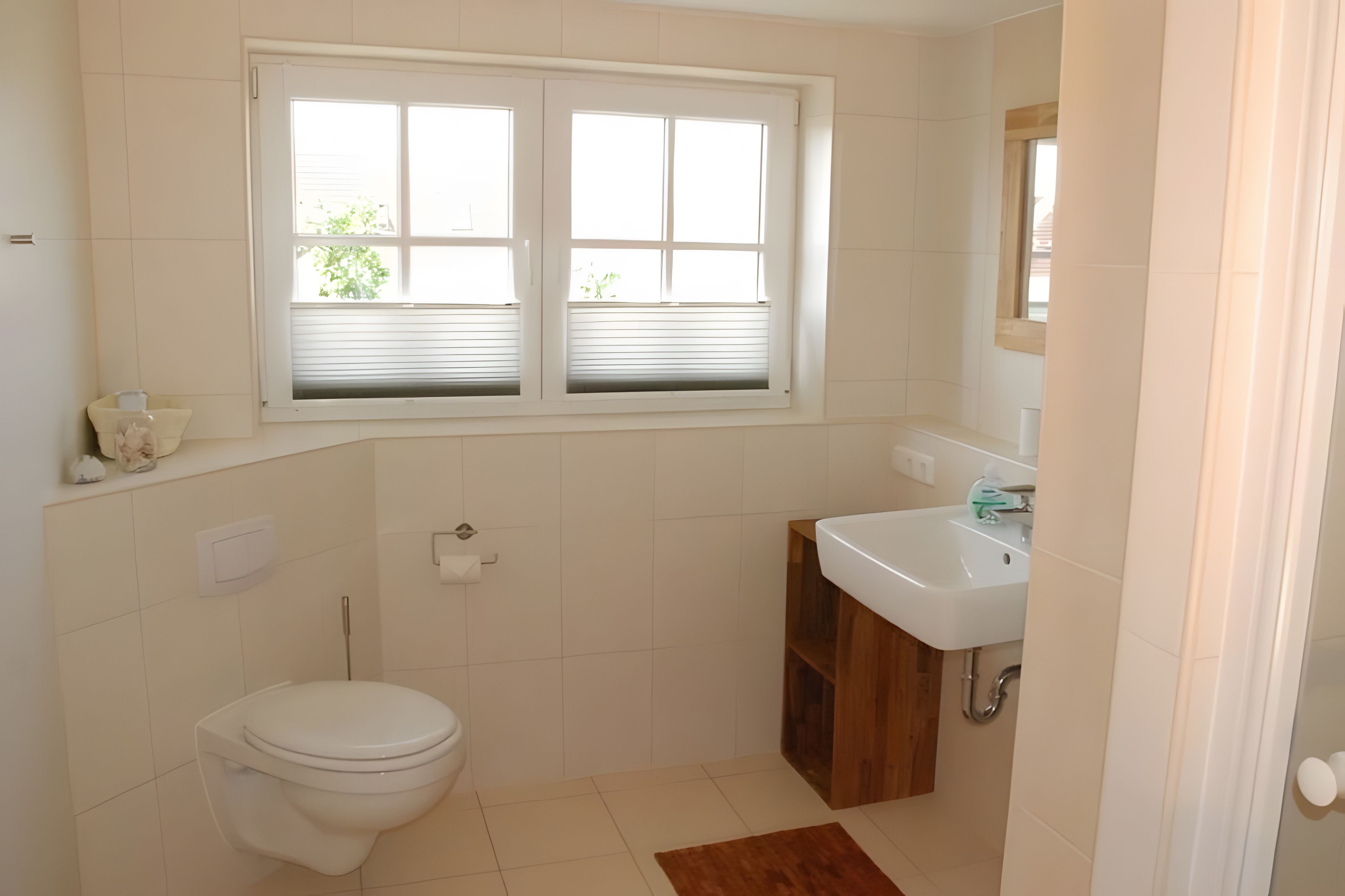 A bathroom with a toilet, a sink, a window, and a mirror.