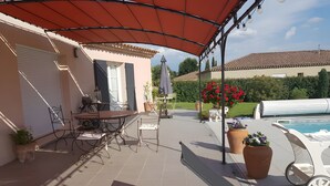Ein überdachter Patio-Bereich mit Tisch und Stühlen, einem Pool und Kübelpflanzen.