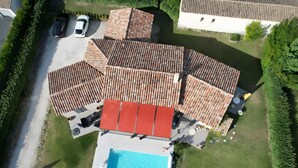 Eine Vogelperspektive eines Wohnhauses mit Swimmingpool, mehreren Dachbereichen und einer Auffahrt mit geparkten Autos.