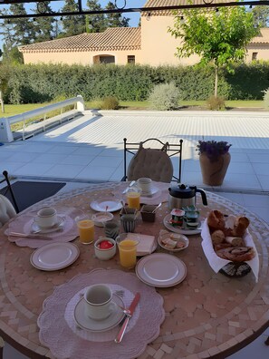 A breakfast table set outdoors with plates, cups, and a basket of bread. - Bed and Breakfast 'Chambre Modigliani' with Mountain View, Wi-Fi and Air Conditioning (Saumane de Vaucluse)