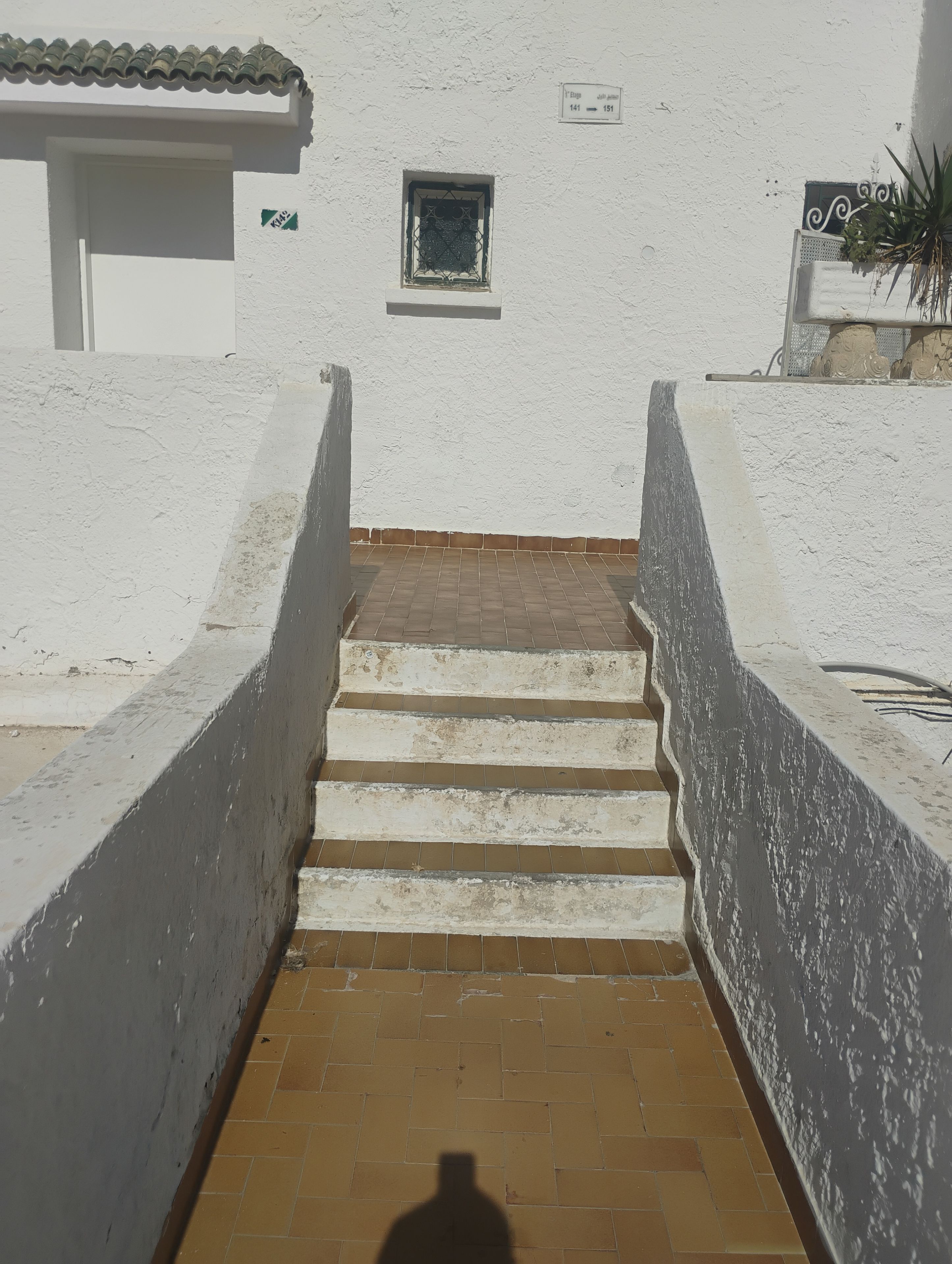 Um conjunto de degraus externos leva a um edifício com fachada branca e uma pequena janela.