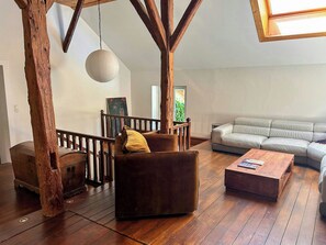 A spacious living area with a wooden staircase, a sofa, a coffee table, and a hanging light fixture. - Old Jura farmhouse in the heart of the Haut-Jura (Châtel-de-Joux)