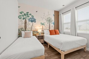 Ein Schlafzimmer mit zwei Betten, einem Nachttisch, einer Lampe und einer Wandmalerei von tropischer Vegetation.