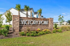 Un letrero que dice 'Victory Point', con un muro de ladrillo y jardín ajardinado.