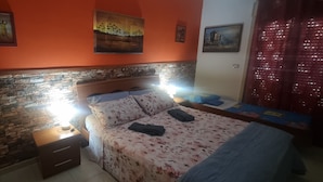 A bedroom with a brick-patterned headboard, a bed with floral bedding, a nightstand with a lamp, and artwork on the walls. - Apartment 'Casa in Complesso Sonia' with Private Terrace (Santa Teresa di Riva)