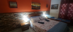 Een slaapkamer met een hoofdeinde van baksteenmotief, een bed met bloemenbeddengoed, een nachtkastje met een lamp en kunstwerken aan de muur.