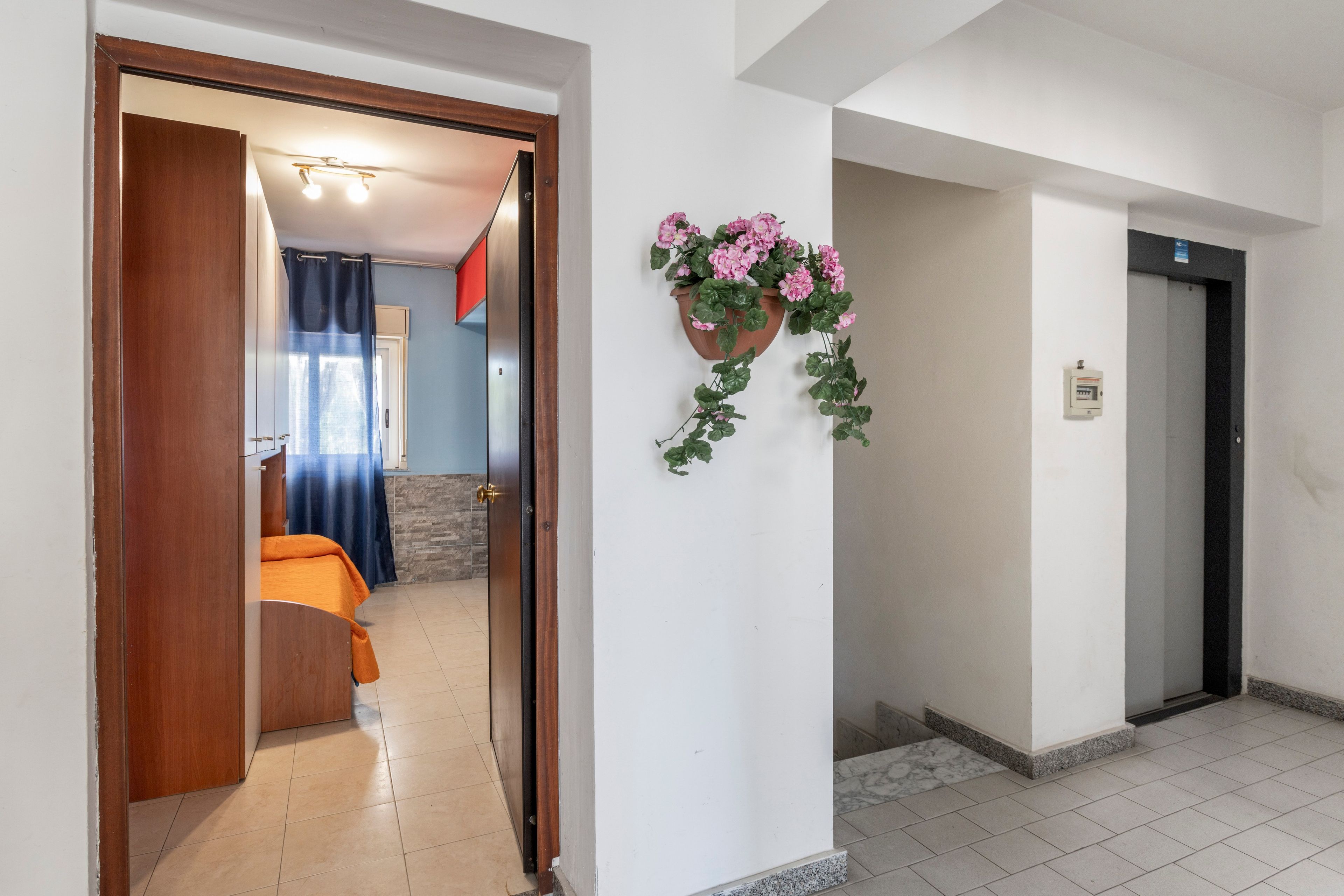 A hotel room with a bed, a bathroom, and a hallway leading to an elevator.