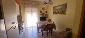 A dining area with a table covered by a patterned tablecloth, chairs, a television, and a painting on the wall.