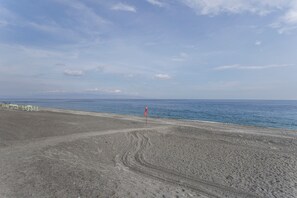 Una platja amb una bandera que assenyala un punt d'interès, cel blau clar i mar tranquil·la.