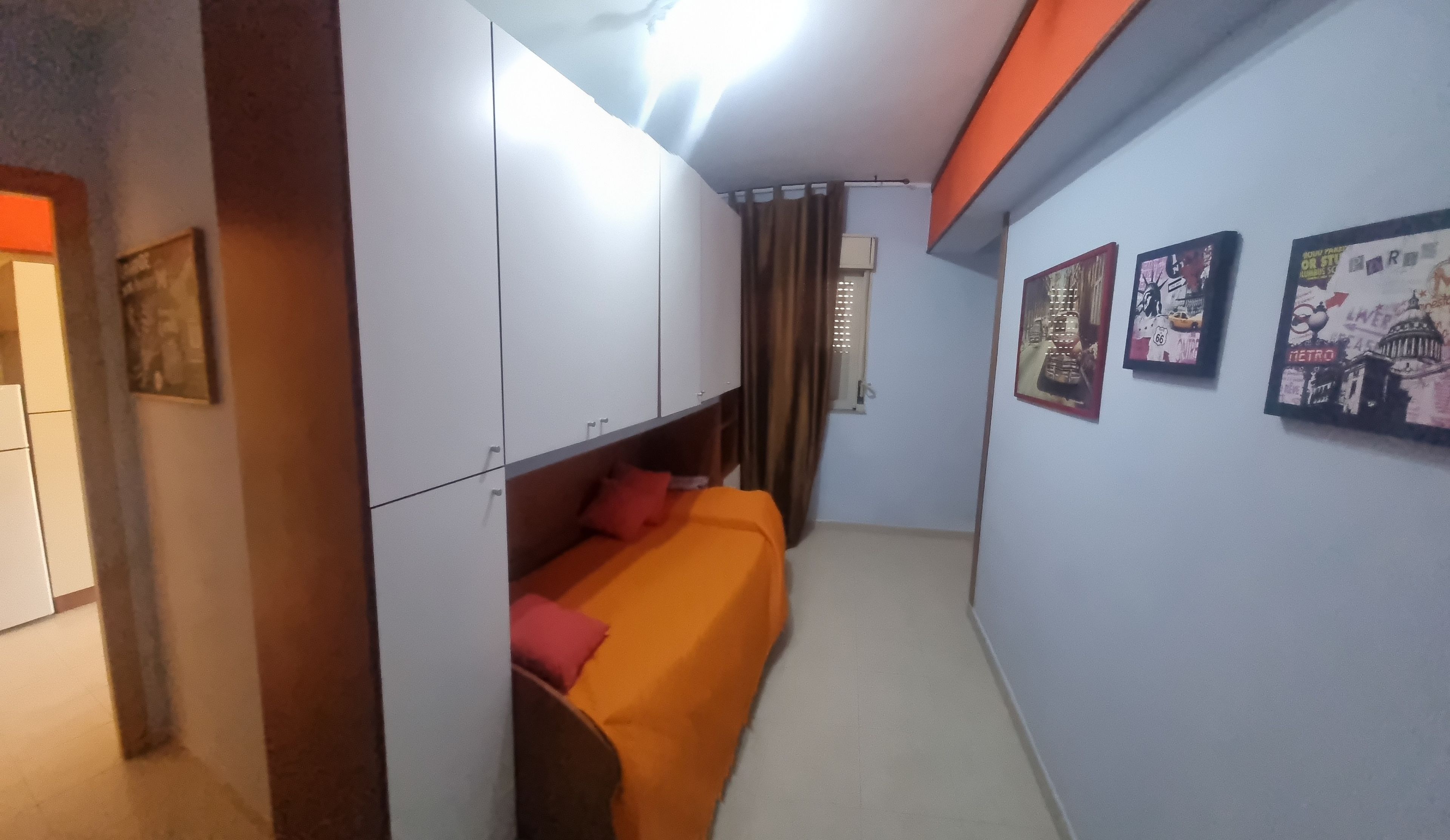 Ein Zimmer mit Bett, Kleiderschrank und Wandbildern.