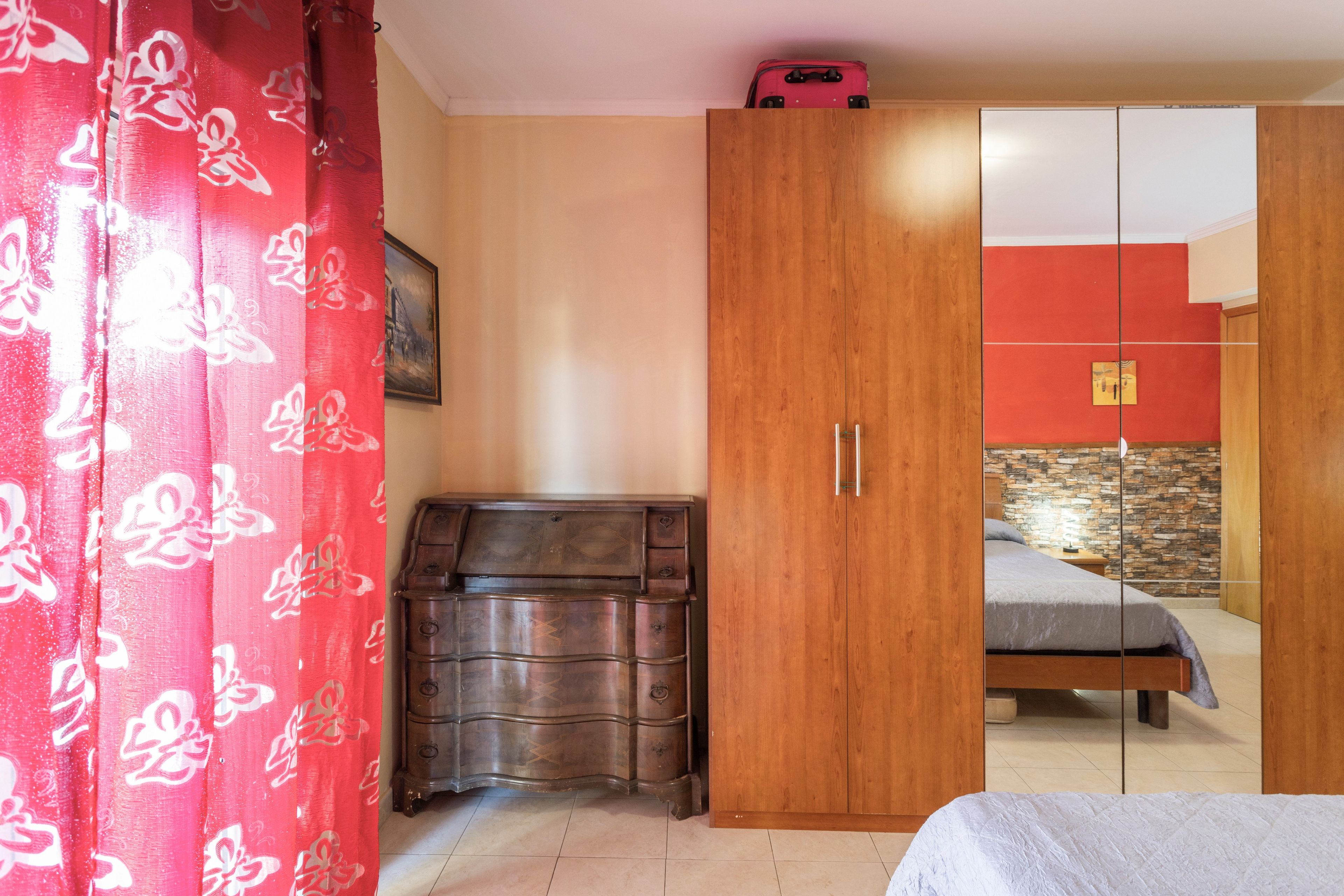 A bedroom with a bed, a wardrobe, a dresser, and a red curtain.