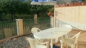 An outdoor patio with a table and chairs, a blue umbrella, and a view of greenery and mountains. - Apartment 'Casa in Complesso Sonia' with Private Terrace (Santa Teresa di Riva)