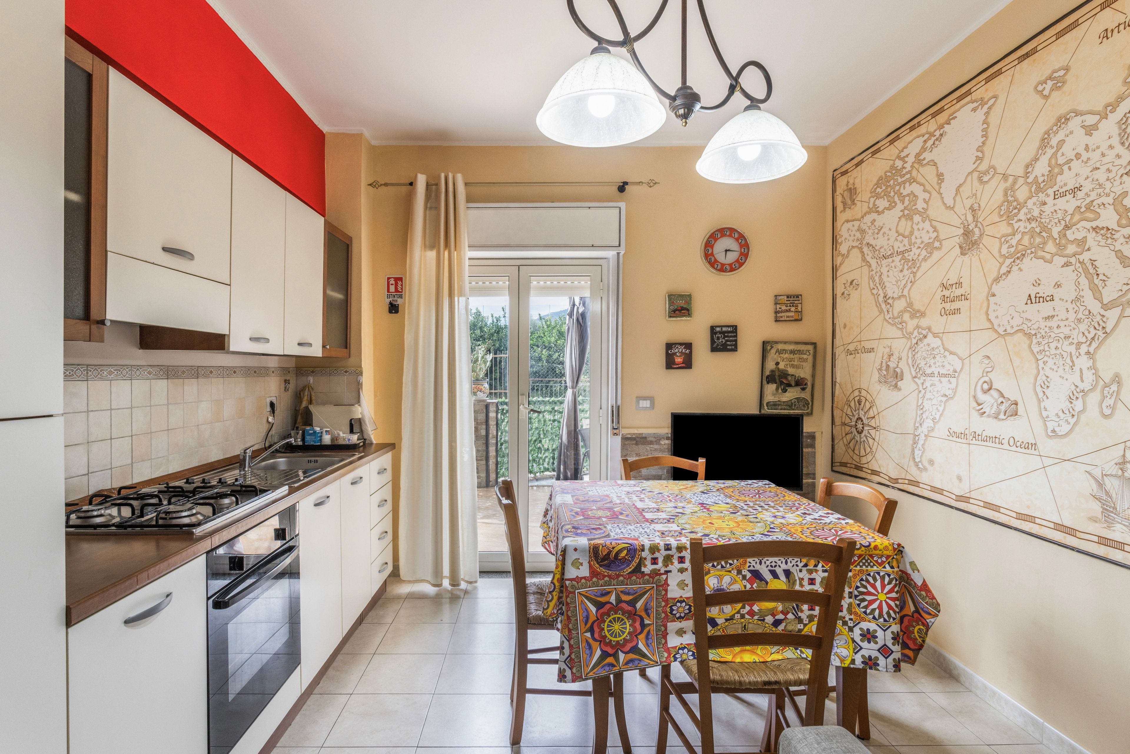 Een keuken met een gasfornuis, oven en een eethoek met een tafel en stoelen. Er hangt een grote kaart aan de muur en er staat een klok.