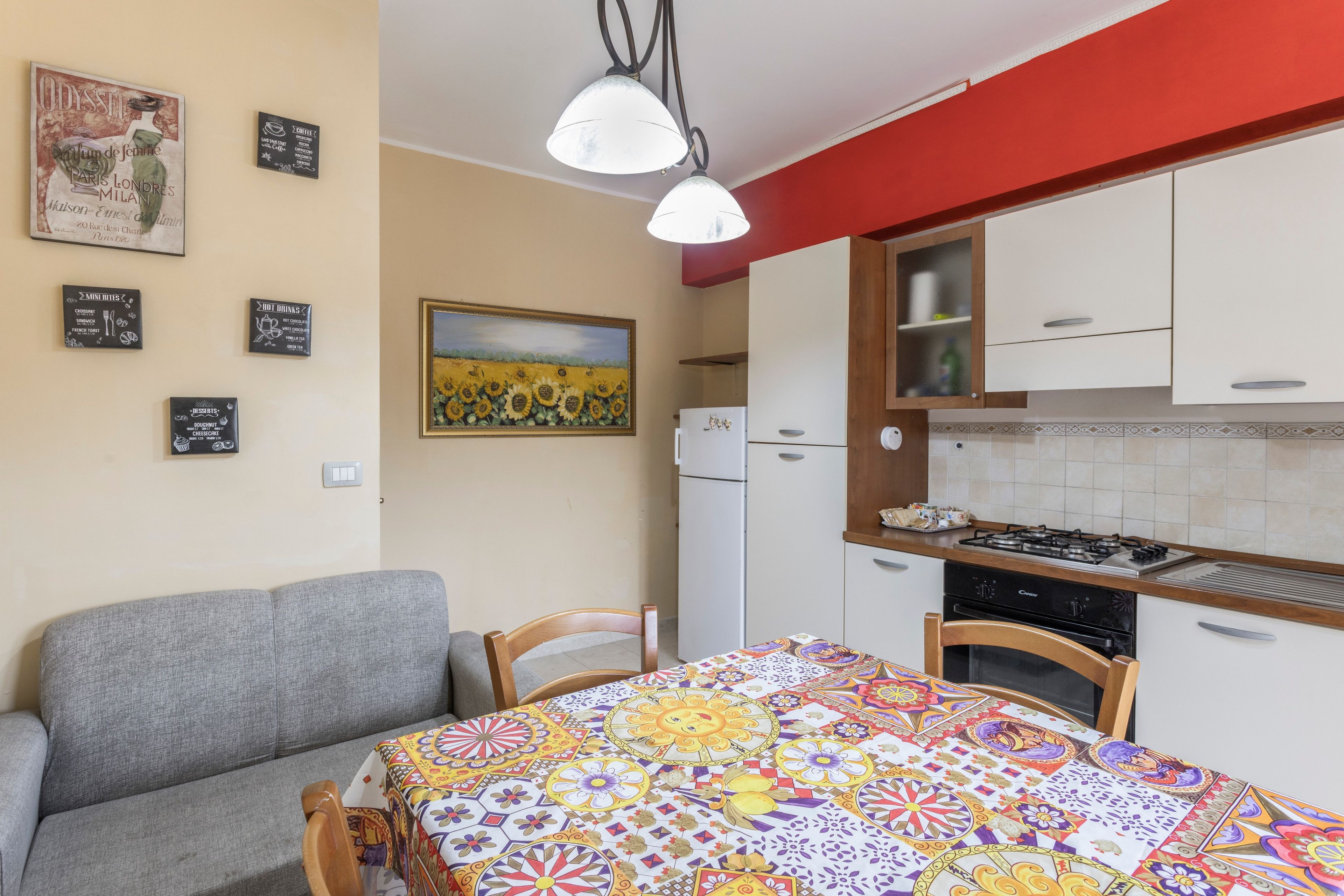 A compact kitchen with a dining area, a refrigerator, a stove, and a wall-mounted light fixture.