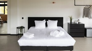 A neatly made bed with white linens, a black headboard, and a small bedside table with a plant and a kettle. - Large Room in Rijswijk (Rijswijk)