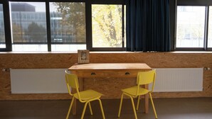 A room with a wooden desk, two yellow chairs, a window with a view of trees, and a radiator. - Large Room in Rijswijk (Rijswijk)