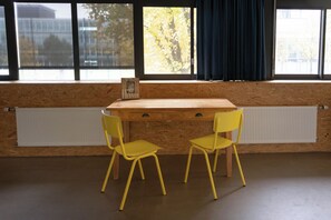 Ein Zimmer mit einem Holztisch, zwei gelben Stühlen, einem Fenster mit Blick auf Bäume und einer Heizung.