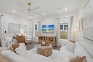 A spacious living room with a white color scheme, featuring a large sofa, a coffee table, and a painting of a beach scene. - Golf Cart, Large Pool, Hot Tub, Walk 2 Beach, Bikes (Santa Rosa Beach)