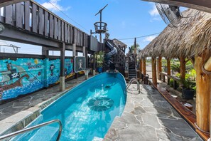 Ein Swimmingpool mit Rutsche, umgeben von Holzkonstruktionen und Wandgemälden.