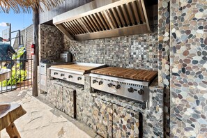 Eine Außenküche mit Steinrückwand und integriertem Grill.