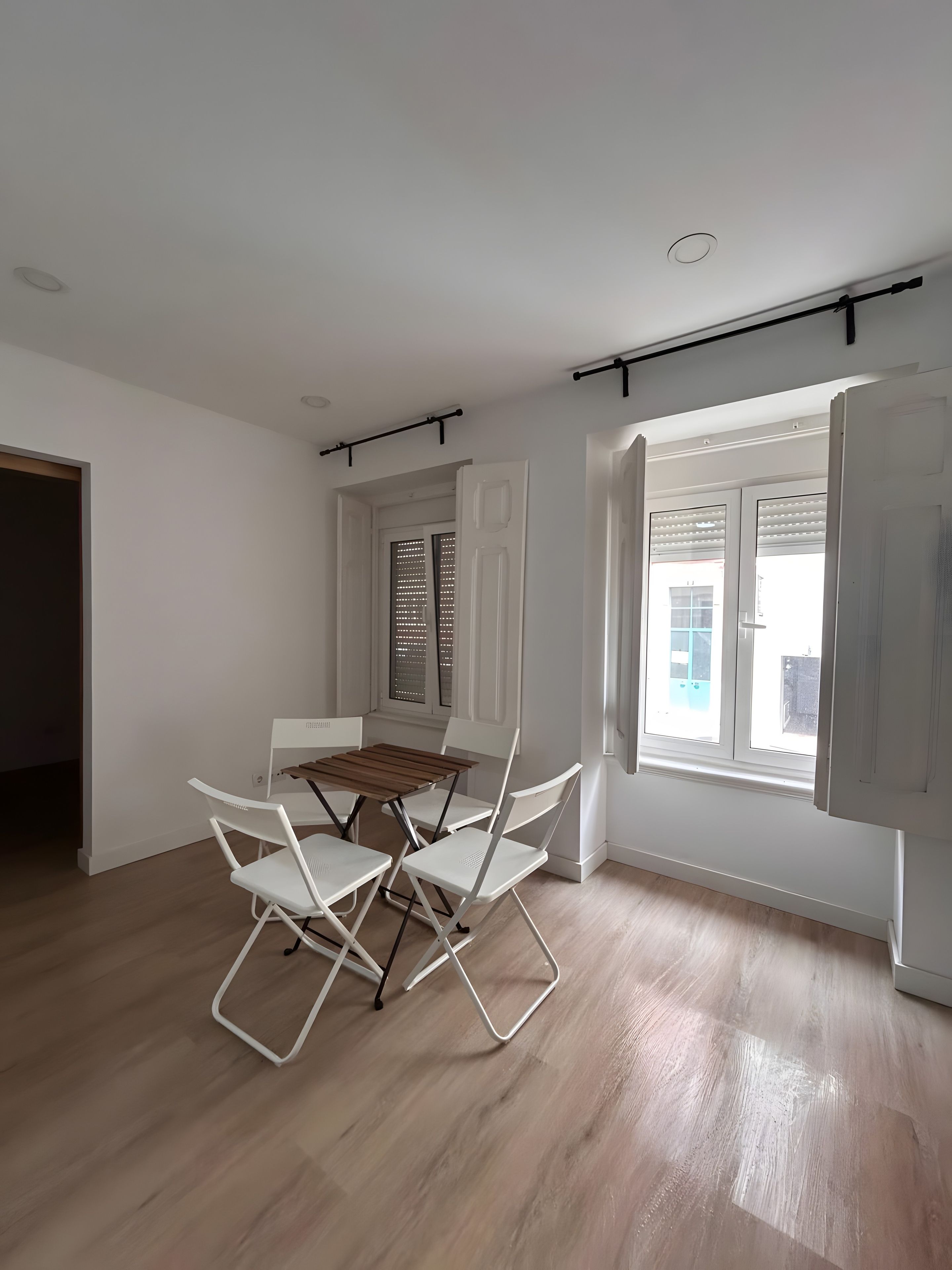 Een kamer met een eettafel en stoelen, een raam met jaloezieën, en een deur.