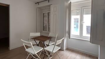 Een kamer met een eettafel en stoelen, een raam met jaloezieën, en een deur.
