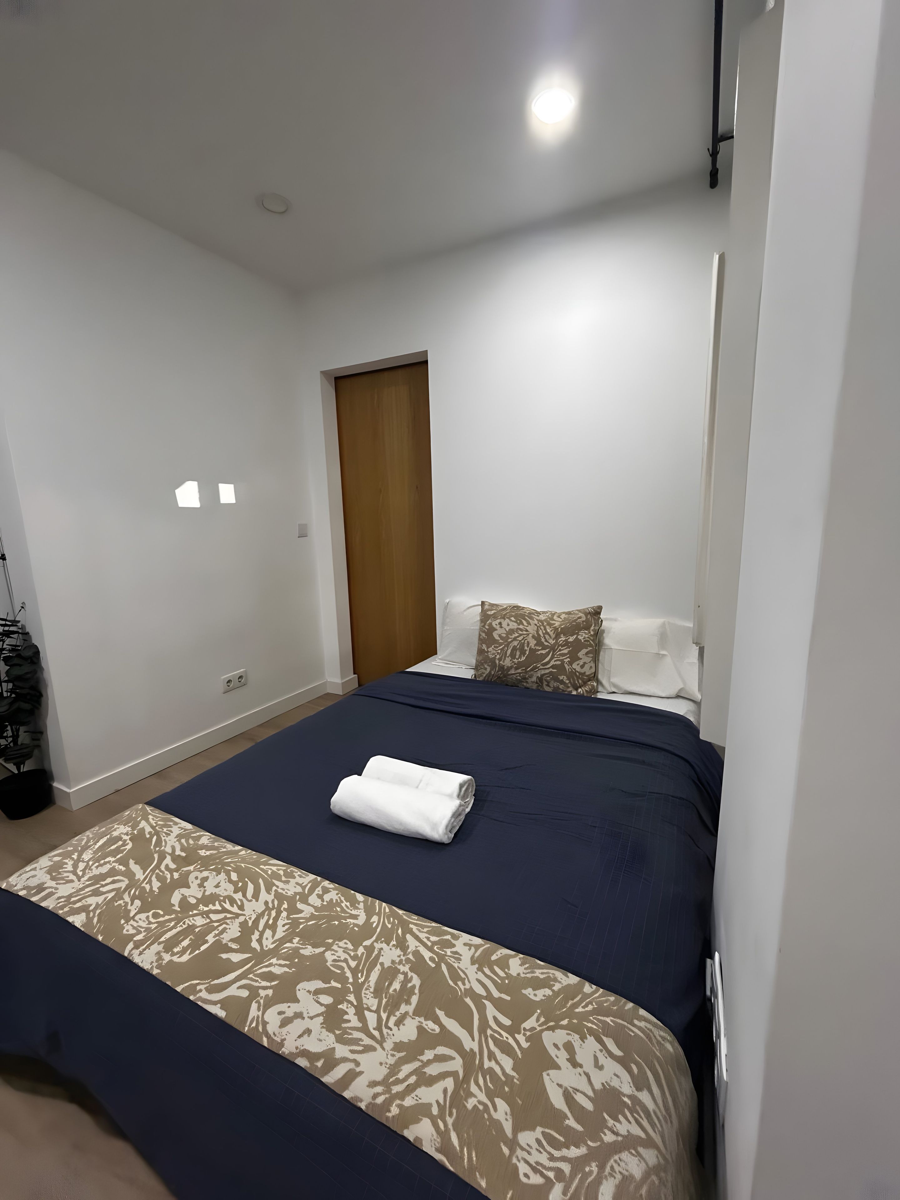 Un dormitorio con cama, una puerta de madera y pared blanca.