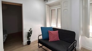 A modern living room with a black sofa, a small potted plant, and a window with blinds. - Holiday Home 'Lisboa Guest House' with Wi-Fi (Lisboa)