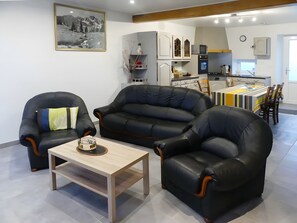 A living room with a sofa, armchairs, and a coffee table. There is a kitchen in the background with a dining area. - Holiday Home 'Les Hirondelles' (Saint-Georges-Lagricol)