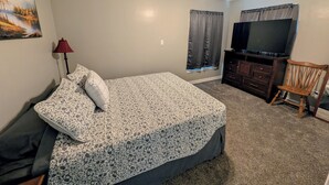 Un dormitorio con cama, ventilador de techo, televisor, cómoda, una silla y ventana con cortinas.