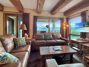 A hotel room with a leather sofa, a wooden coffee table, and a view of a mountainous landscape through large windows. - New Listing - The Plaza 235, Walk to Crested Butte Lifts (Crested Butte)