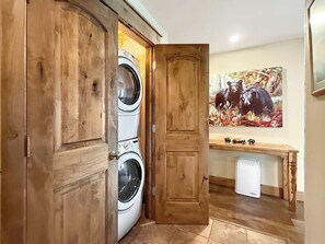 A laundry room with two stacked washing machines, a wooden door, and a bear painting on the wall. - New Listing - The Plaza 235, Walk to Crested Butte Lifts (Crested Butte)