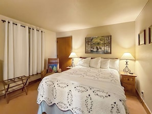 A bedroom with a large bed, two bedside tables with lamps, a chair with a cushion, a wooden door, and a painting on the wall. - New Listing - The Plaza 235, Walk to Crested Butte Lifts (Crested Butte)