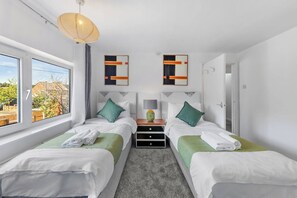 A hotel room with two beds, a window, a lamp, and artwork on the walls. - Welcome to our 3-bedroom home in Camberley, Surrey, perfectly equipped for up to 5 guests. Ideal for business travelers, contractors, families, relocation stays, and group trips. (Surrey)