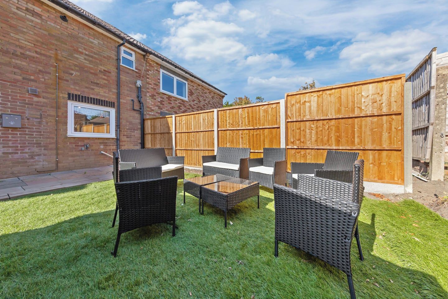 A backyard with a brick house, a wooden fence, and outdoor furniture including chairs and a table.