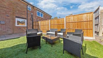 A backyard with a brick house, a wooden fence, and outdoor furniture including chairs and a table.