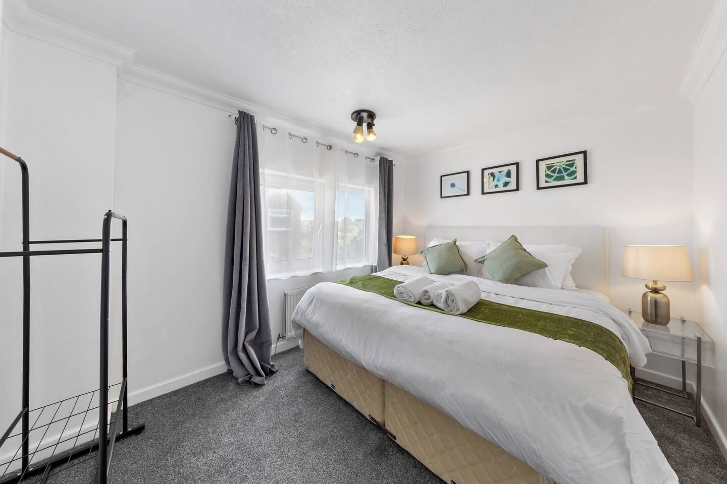 A hotel room with a bed, two bedside lamps, a window with curtains, and a radiator.