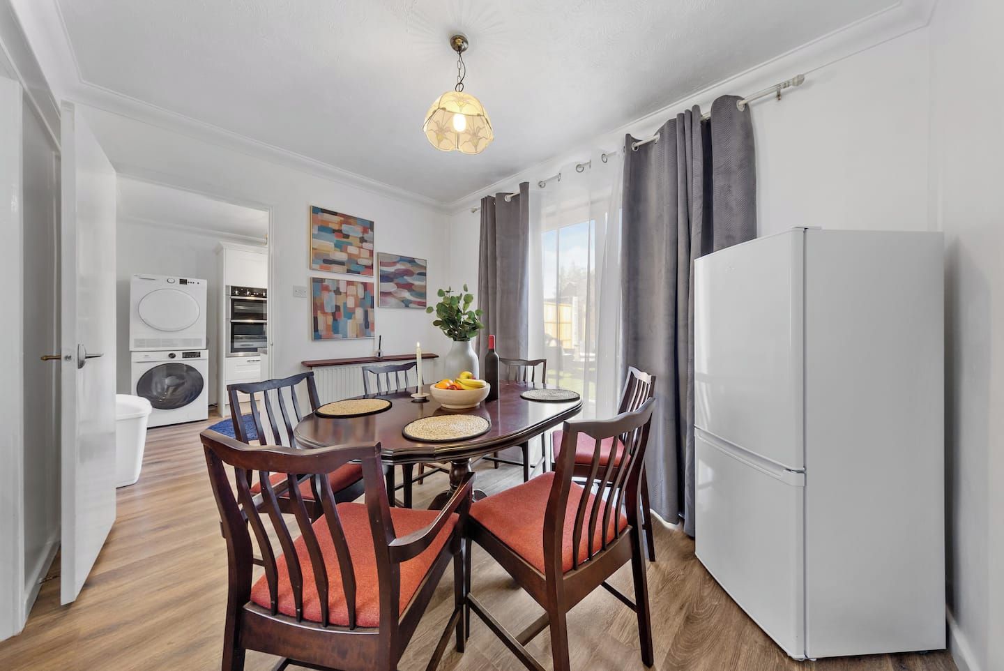 Un área de comedor con una mesa redonda, sillas, un refrigerador blanco y una lavadora al fondo.