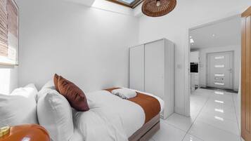 A modern bedroom with a skylight, a bed with white and brown bedding, a wardrobe, and a bathroom visible in the background.