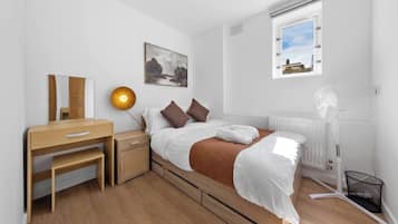 A bedroom with a bed, bedside table, lamp, and a window with a view.