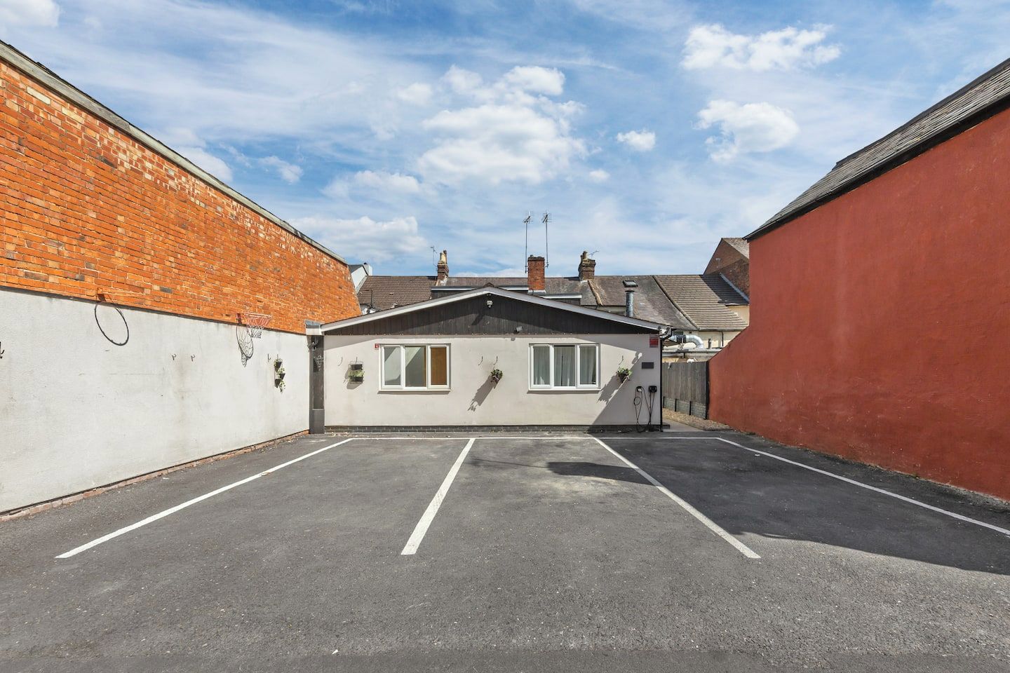 A parking lot with a small building, a brick wall, and a red wall.