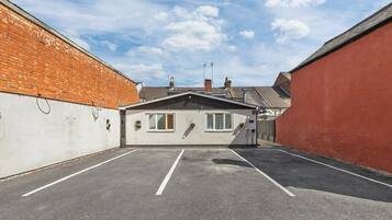 A parking lot with a small building, a brick wall, and a red wall.