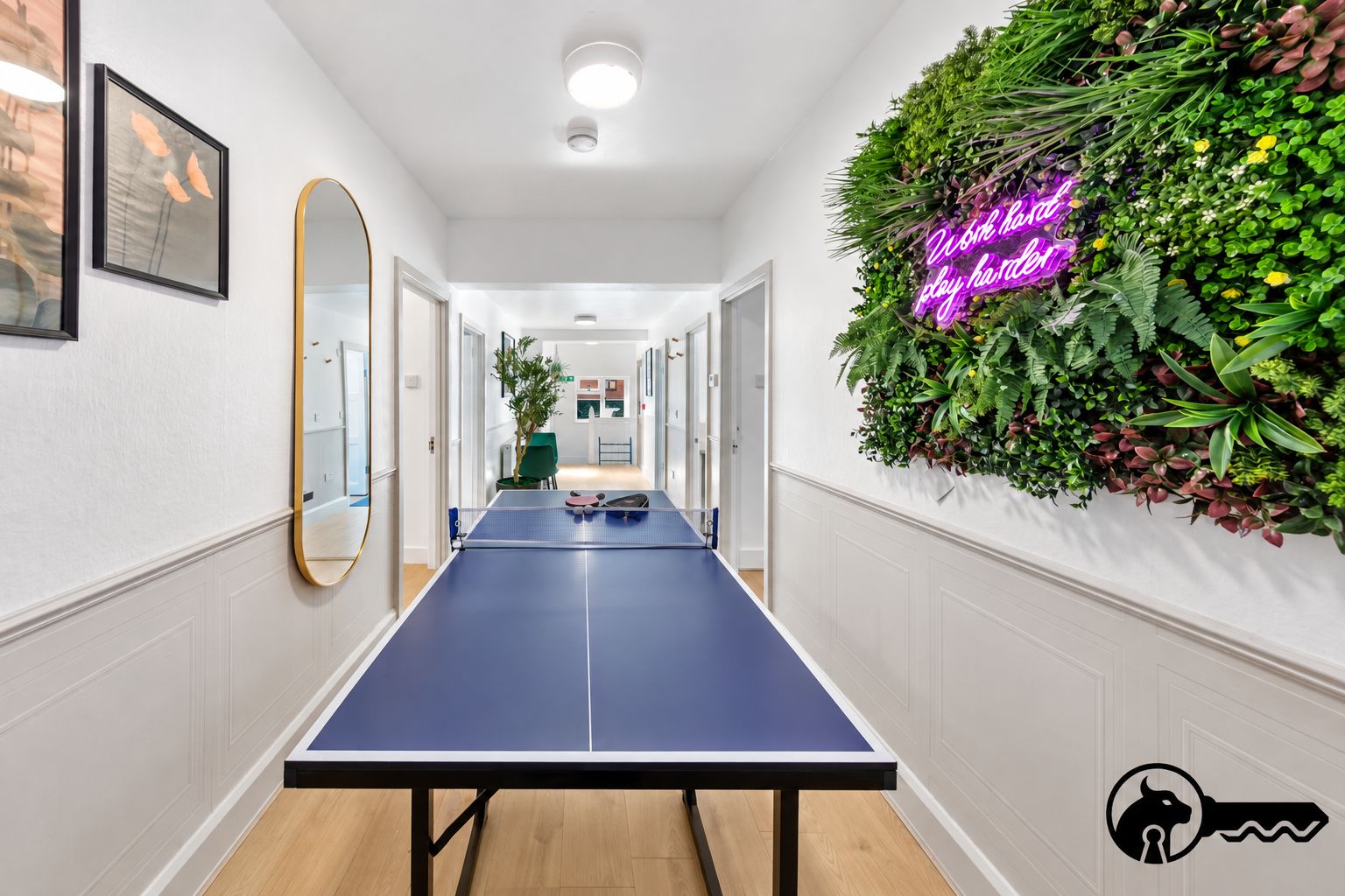 A hallway with a ping pong table, a neon sign, and a wall-mounted plant arrangement.
