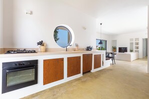 A modern kitchen with a central island, built-in oven, and a round mirror above the countertop. - Villa Marevento by Perle di Puglia (Carovigno)