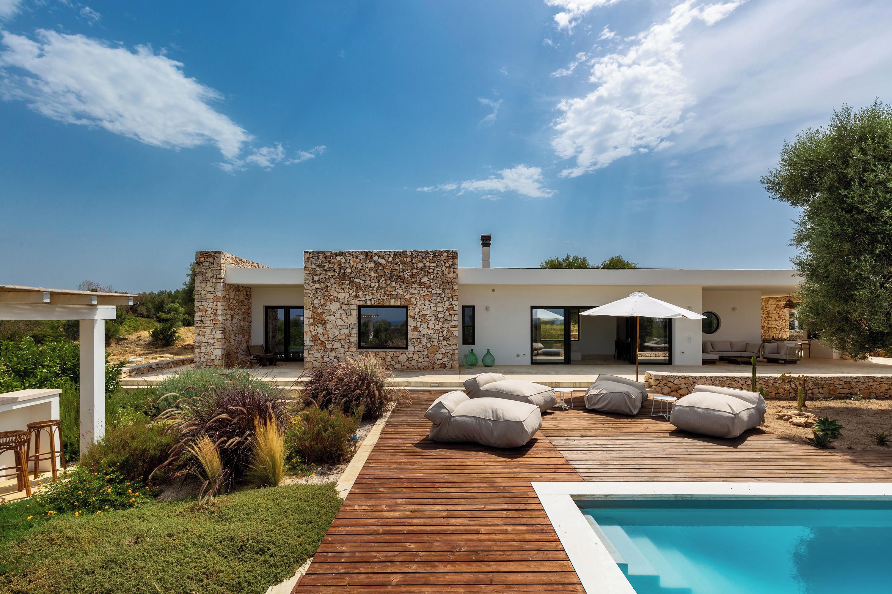 A modern house with a pool, outdoor seating, and a stone facade.