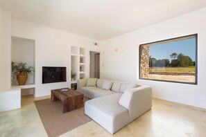 Un salon moderne avec un canapé d’angle, une table basse en bois et une grande fenêtre donnant sur un mur en pierre et de la verdure.