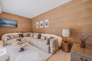 A modern living room with a sectional sofa, a coffee table, and a lamp. There are framed pictures on the wall and a painting above the sofa. - Paradisa Summit - Luxurious penthouse apartment with Mont-Blanc views (Chamonix-Mont-Blanc)