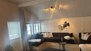 Uma sala de estar moderna com um sofá seccional, uma mesa de centro redonda e uma pintura grande na parede.