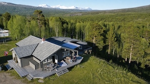 Una casa moderna con terraza, rodeada de bosque y montañas al fondo.
