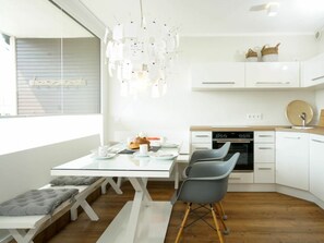 Eine moderne Küche mit weißen Schränken, einem eingebauten Backofen und einem Essbereich mit einem Glastisch und grauen Stühlen.